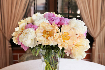 Bouquet of yellow, white and pink peonies in a vase on the table