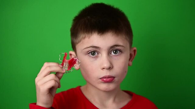 A 9-year-old boy is holding a dental alignment plate, an abomination and a demonstration of a dental alignment plate.