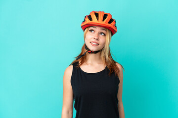Young cyclist girl over isolated blue background thinking an idea while looking up