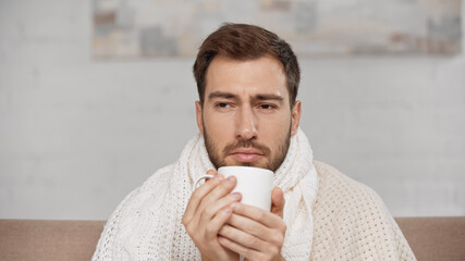sick man wrapped in blanket holding cup of tea