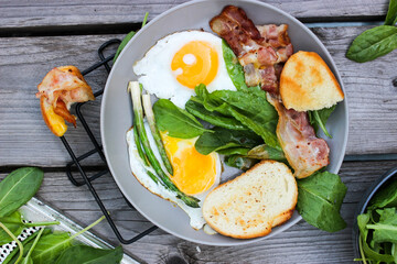 Breakfast on a plate of scrambled eggs with toasted bread, bacon and aromatic herbs