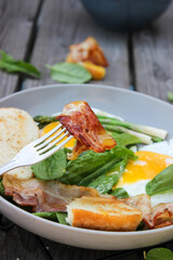 Breakfast on a plate of scrambled eggs with toasted bread, bacon and aromatic herbs