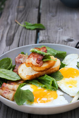 Breakfast on a plate of scrambled eggs with toasted bread, bacon and aromatic herbs