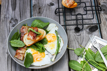 Breakfast on a plate of scrambled eggs with toasted bread, bacon and aromatic herbs