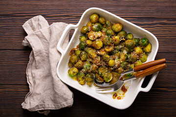 Healthy vegetarian dish roasted brussels sprouts with butter and parmesan cheese in white ceramic casserole top view on dark rustic wooden table from above, vegan food  