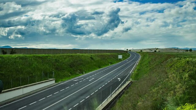 A time lapse over an asphalt-covered highway with speeding cars and rolling clouds in the sky shot in 4K