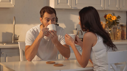 bearded man drinking coffee and looking at blurred girlfriend