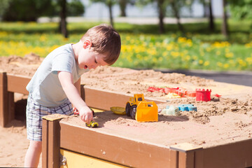 A baby boy plays with toys, cars in the sand on the playground