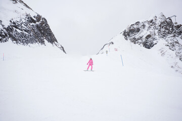 Girl in a pink suit on a snowboard against the backdrop of mountains