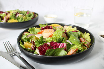 Grilled shrimp, lettuce, orange, red onion on a white plate, close-up. Fried shrimps. Healthy salad. Fresh summer salad with shrimps and a mix of green leaves. Fresh seafood recipe.