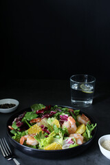 Fresh summer salad with shrimps, mix of green leaves and sesame seeds on a dark background, side view, copy space. Seafood salad recipe.