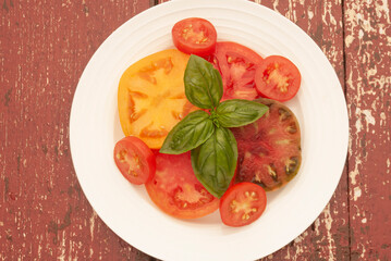 Variety of freshly picked and sliced tomatoes with sprig of basil on a white plate