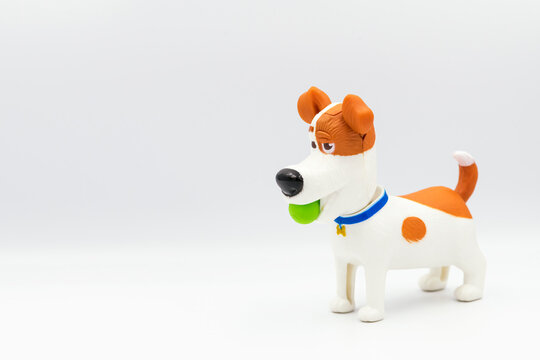 A Statuette Of A Dog Playing With Ball Isolated On A White Background. Dog In Profile From The Side. Figure And Children's Toy In The Form Of A Dog.