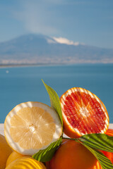 Citrus fruits from Italy: tarocco oranges and lemons with blue sea and Mount Etna in the background - 437451672