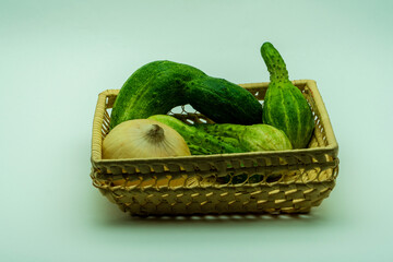 Four deformed cucumbers and onion lie in wicker basket. Organic vegetables is good for eat. It's contains vitamins and microelements. Horizontal white background image.