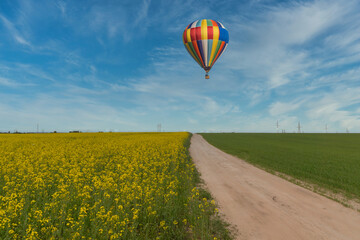 Spring field of blooming rapeseed to the horizon and a balloon flying over it.