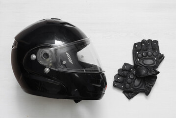 Black motorcycle helmet and gloves on the white flat lay background.