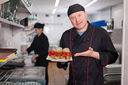 Portrait of confident chef working in restaurant kitchen, showing right off stove dish