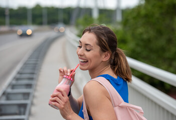 Girl drinking strawberry milkshake outdoors after workout.