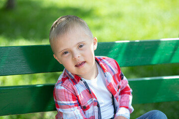 Happy boy with Down syndrome in the park against a background of green grass, close-up portrait of...