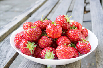 Fresh red strawberries in the white bowl in the grass in the garden. Clean, delicious and ready to eat.