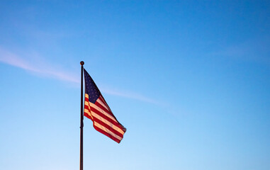 The American flag flies under blue skies as the sun goes down.