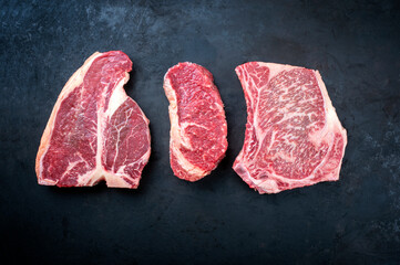 Raw dry aged wagyu porterhouse beef steak, entrecote and cutlet offered as top view on a rustic...