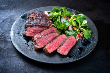 Modern style traditional dry aged sliced wagyu roast beef with corn salad and pine nuts served as close-up on a Nordic design plate