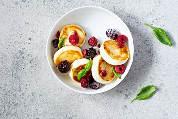 Fresh cottage cheese or ricotta  pancakes (syrniki,fritters) on a white plate with fresh berries on a blue background. Delicious healthy breakfast.  Ukrainian, Russian cuisine sweet food.