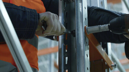 close up of warehouse worker in uniform with wrench during rack arrangemen
