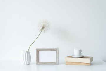 Empty wooden picture frame mockup. White vase with shower head, books and cup of coffee. Elegant...