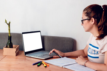 girl with glasses who is working from home and is checking her computer and taking notes on a notepad