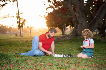 dad and child play logic game. father and son playing chess on grass in park. fathers day