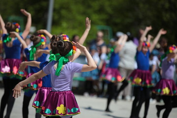 A group of little girls in colorful dresses with beautiful hairstyles dance at an outdoor festival.Kids party