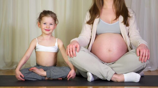 Woman and child little girl meditate together on mat. Mother pregnant do yoga on rug with daughter toddler. happy healthy family. Sports exercises at home. Health care. smiles second pregnancy mom.