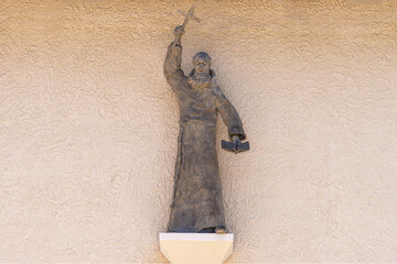 Santa Inez, CA, USA - May 26, 2021:San Lorenzo Seminary. Closeup of gray preaching monk statue on beige wall above main entrande door to the church - obrazy, fototapety, plakaty