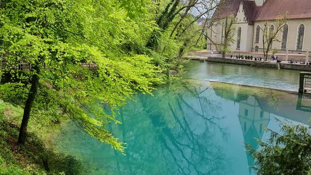 Scenic view of a Catholic monastery in the village of Blaubeuren, Germany. A Catholic monastery and the surrounding trees are reflecting in the turqoise-blue colored water.