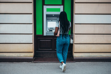 Attractive african american woman using credit card and withdrawing cash at the ATM - Powered by Adobe