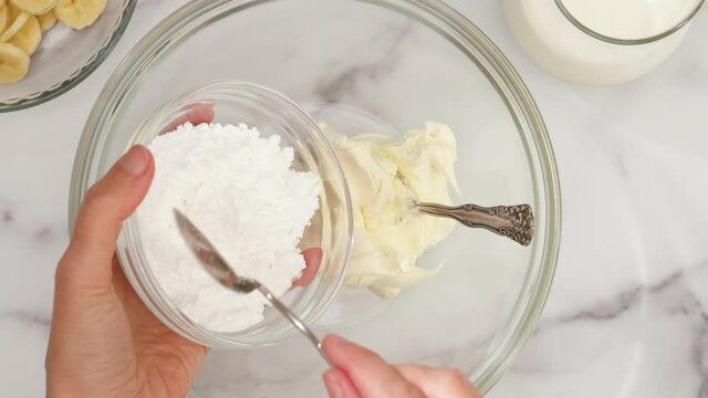 Cream cheese and powdered sugar in a bowl. Ingredients for whipped cream cheese dessert close up, woman hands, flat lay