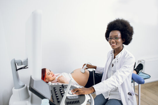 Medicine, healthcare and ultrasound concept. Pregnancy and obstetrics. Happy satisfied afro-american woman doctor, providing ultrasound screening for young pregnant woman patient