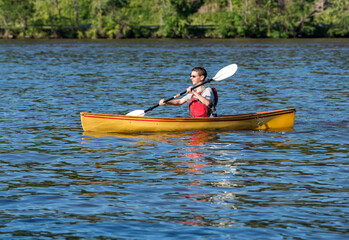 Young man in lifejacket paddling a pack canoe using a kayak paddle on a lake in West Virginia - Powered by Adobe