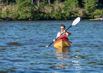 Young man in lifejacket paddling a pack canoe using a kayak paddle on a lake in West Virginia