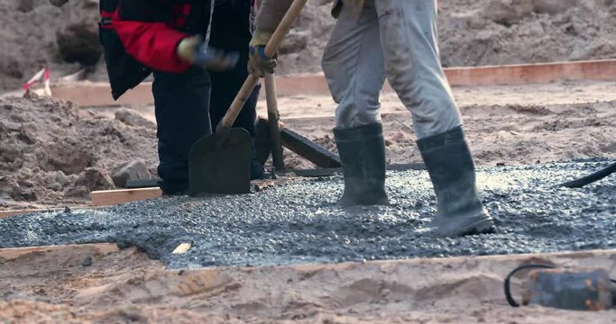 Professional construction workers are leveling wet cement with shovels, 4k