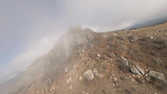 Shooting from sports fpv drone flying over mount Katyusha with dense natural fog over small touristic village city. Aerial shot natural cliff with face of Ekaterina image at nature landscape blue sky