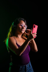 Mujer latina escuchando música con auriculares y un celular rojo en fondo negro