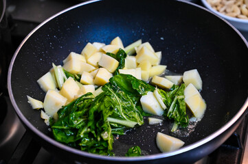 Cooking spinach and potatoes in pan in kitchen.