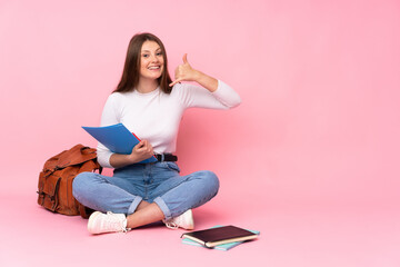 Teenager caucasian student girl sitting on the floor isolated on pink background making phone gesture. Call me back sign