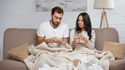 Fototapeta premium caring young woman holding glass of water near sick man in living room