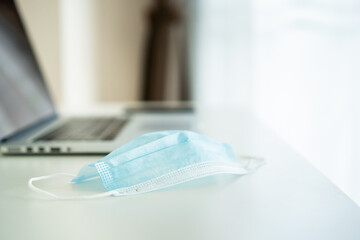 Hygiene protective face mask and laptop computer on the table in home office.