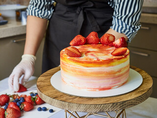 Woman pastry chef decorates cake with strawberries. Home confectionery, small business.
